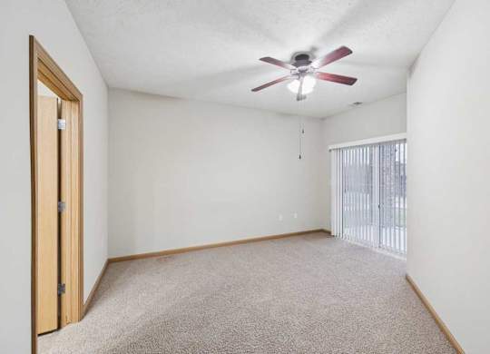 Spacious bedroom with plush carpet, ceiling fan, and sliding glass door to private balcony or patio.