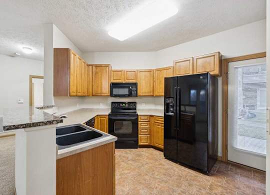 Kitchen with natural wood cabinets, black appliances, double-basin sink, and door to private balcony.