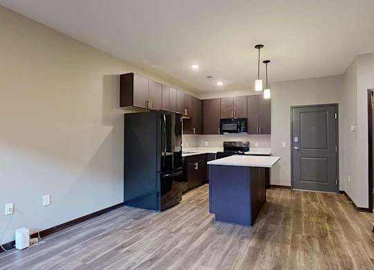 an open-concept living room and kitchen with dark cabinets and black appliances