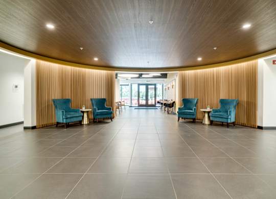 An open apartment lobby with blue chairs and a wooden ceiling.