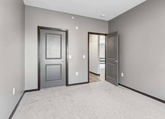 Carpeted apartment bedroom with gray walls, double-door closet access, and an open doorway leading to the hallway.