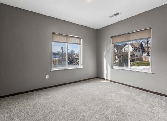 Spacious apartment bedroom with soft carpeting, two large windows, and abundant natural light.