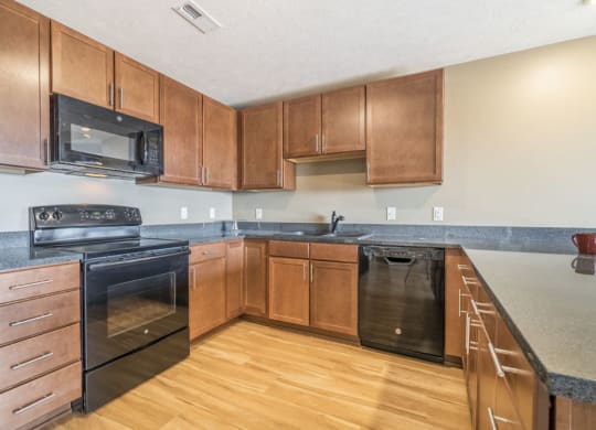 Large U-shaped kitchen with warm brown cabinets, black appliances, grey granite