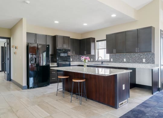 the large community kitchen with dark cabinets and a large island with a granite countertop