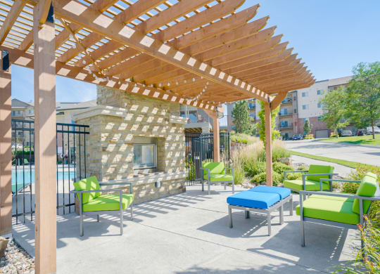 a pergola with green chairs and a blue ottoman in front of a stone fireplace