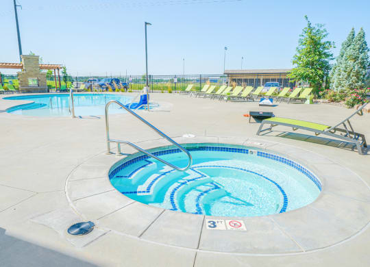 a hot tub with green lounge chairs and trees in the background