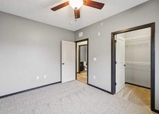 A carpeted bedroom with a walk-in closet and a ceiling fan.