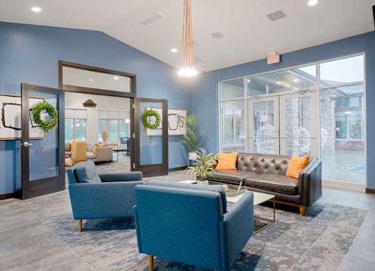 Community lounge with upholstered seating, fireplace, and floor-to-ceiling windows creating a bright, welcoming atmosphere.