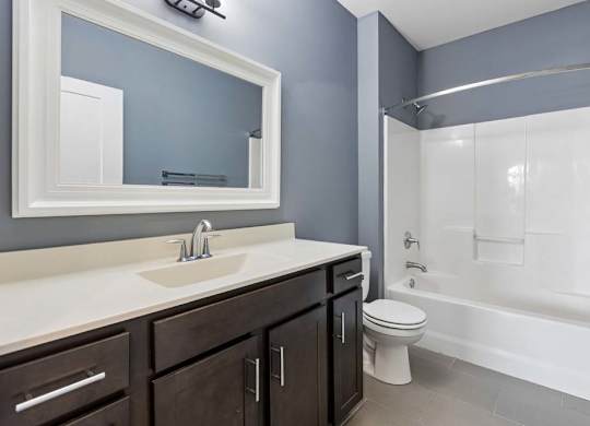 Deep espresso cabinetry and a white vanity top add contrast to this apartment bathroom with gray walls and a tub-shower combo.