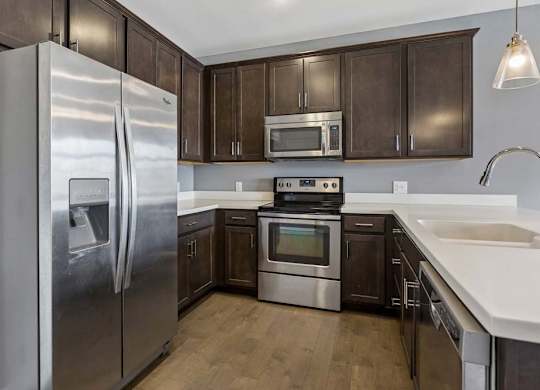 Dark wood cabinetry wraps around this apartment kitchen, paired with white counters, stainless steel appliances, and a peninsula sink.