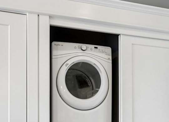 Stacked washer and dryer fit neatly into a recessed apartment laundry closet with white sliding doors and trim.