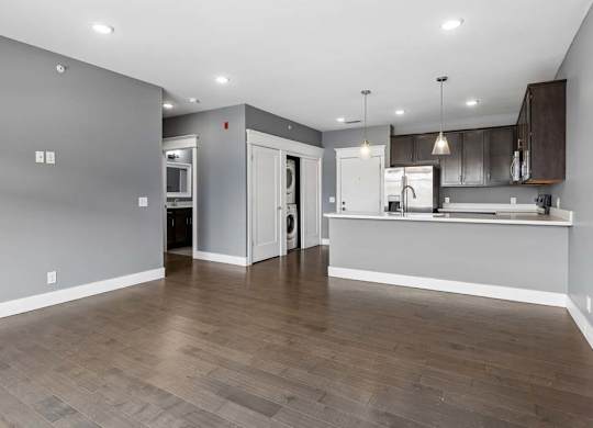Open apartment living area leads into a kitchen with dark cabinetry, a breakfast bar, pendant lighting, and nearby in-home laundry.