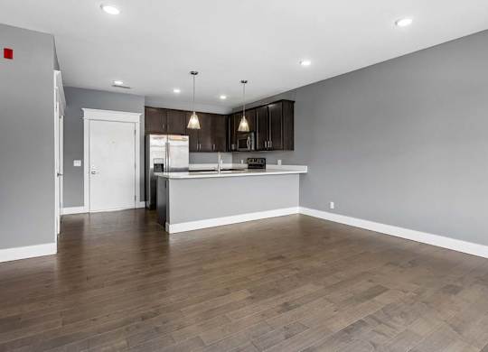 Generous living area with wood-look flooring opens to a dark-cabinet kitchen, breakfast bar, and stainless steel appliances.