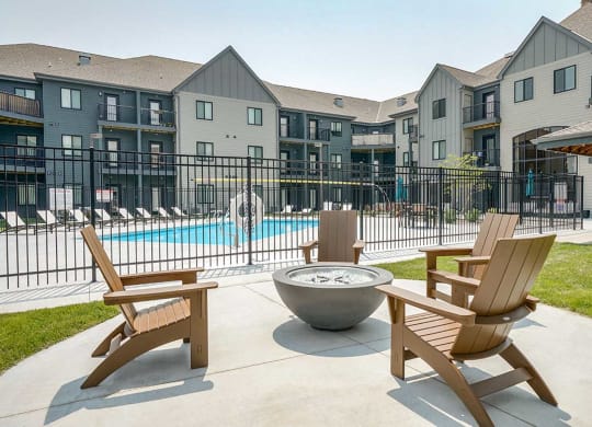 a firepit with Adirondack chairs around it in front of a gated pool area