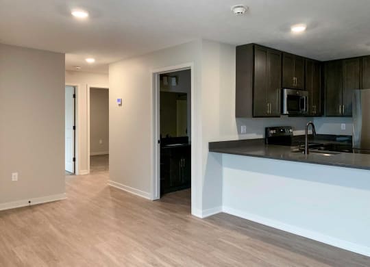 a kitchen with dark cabinets and a living room with wooden flooring