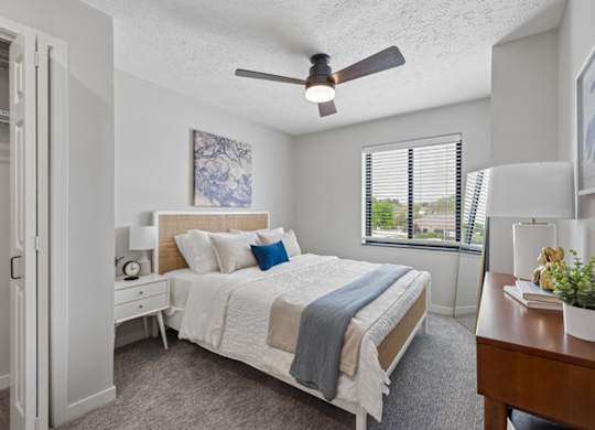 Bright apartment bedroom with ceiling fan and large window.