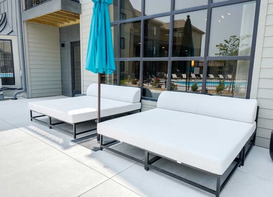 a patio space in front of a large window with two outdoor daybeds and an umbrella