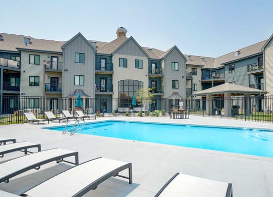 a swimming pool in the center of an apartment courtyard with lounge chairs next to it
