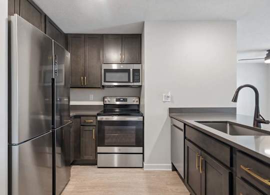 Modern apartment kitchen with dark cabinetry, stainless steel appliances, a deep undermount sink with a pull-down faucet, and a functional open layout.