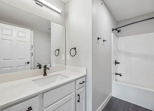 Apartment bathroom with white vanity, black fixtures, and tub-shower combination with surround.