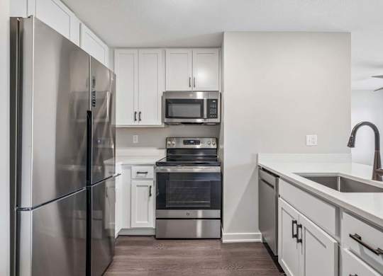Apartment kitchen with white cabinetry, stainless steel appliances, and oversized peninsula with built-in sink.