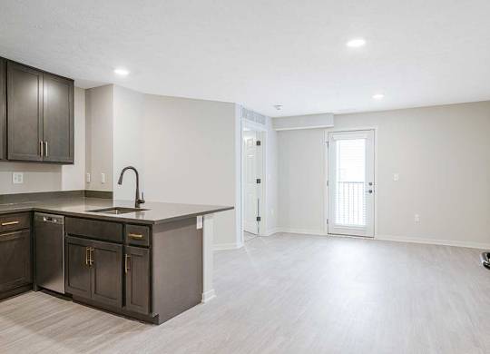 An empty living room and a kitchen with dark cabinets in the Dove at the Knock Apartments in Lincoln, NE