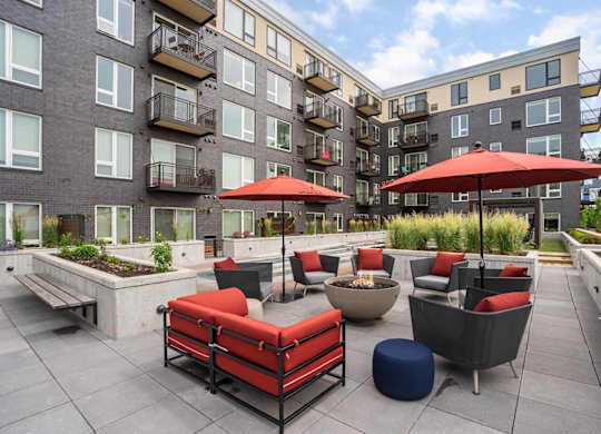 a patio area with red couches and umbrellas surrounding a fire pit in the zen garden