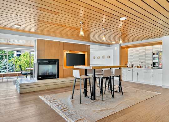 A TV lounge and coffee bar area in the clubhouse sky lounge featuring a large flat-screen TV, fireplace, high-top table with stools, and built-in coffee station.