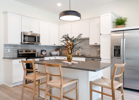 Kitchen with white cabinets and stainless steel appliances three wooden chairs surrounding kitchen island