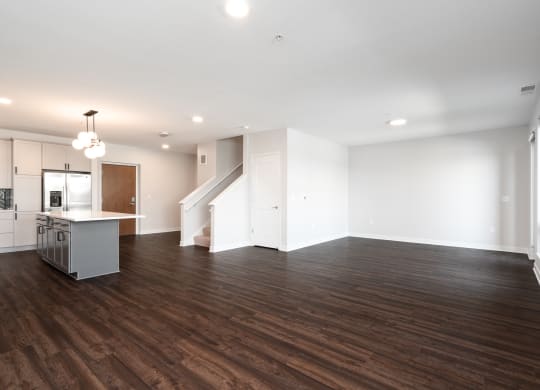 large open living and dining area with dark hardwood flooring. Kitchen counter and staircase to the left.
