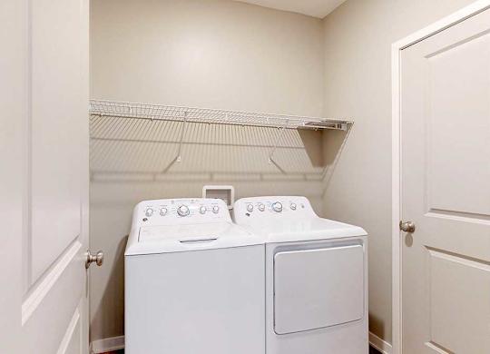 A full-sized washer and dryer in a laundry room, with overhead shelving.