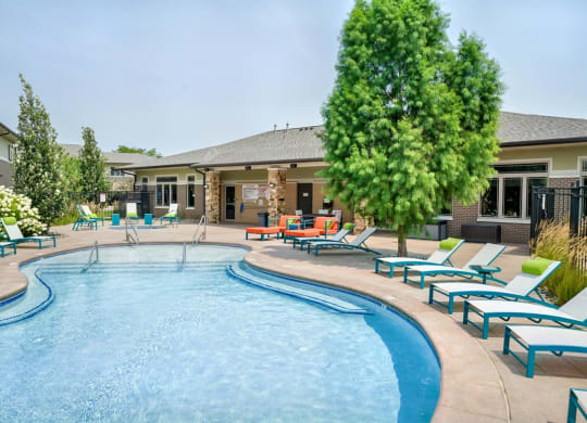 Organically shaped resort style pool surrounded a pool deck with bright blue lounge chairs