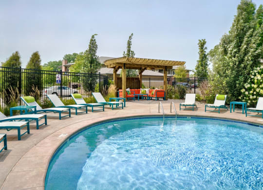Edge of blue pool with lounge chairs around it and wood pergola in the background