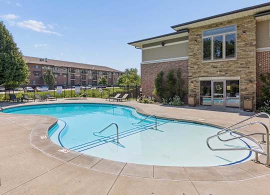 Outdoor swimming pool at Villas of Omaha at Butler Ridge with lounge chairs, entry steps, and the community clubhouse.