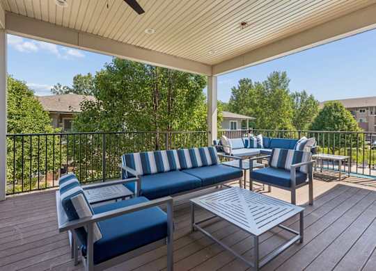 Covered outdoor lounge at Villas of Omaha at Butler Ridge with blue cushioned seating, tables, ceiling fan, and treetop views.