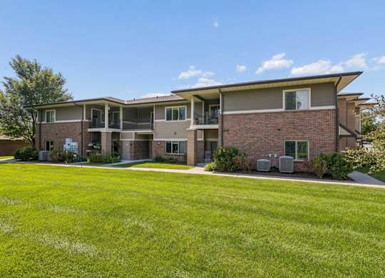 Apartment exterior with brick siding, private balconies, green lawn, and mature landscaping.