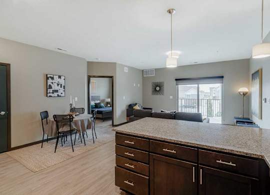 A kitchen with dark wood cabinets and a granite countertop in front of a living room