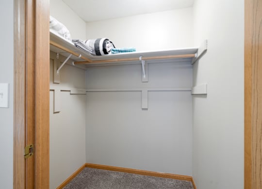 a walk in closet with a white wall and a shelf