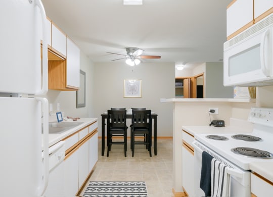 a kitchen with white appliances and a dining room table with chairs in the back