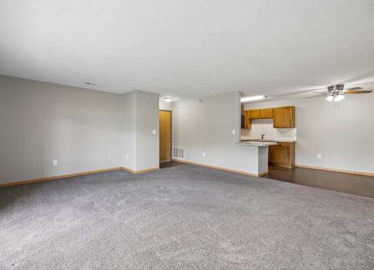 Expansive apartment living room with plush carpeting, an open breakfast bar, and a connected dining area and kitchen.