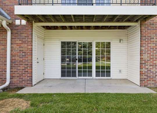 Covered ground-floor apartment patio with a concrete seating area, sliding glass door, and grassy lawn.