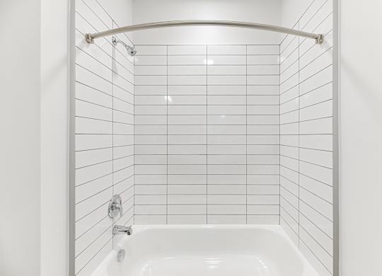 A white tiled bathroom with a white tub and a white shower curtain.