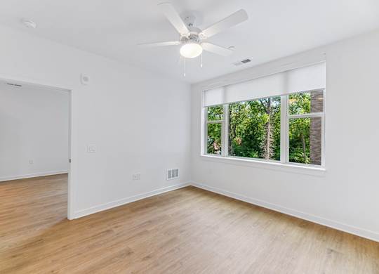 A room with a ceiling fan and a window overlooking trees.