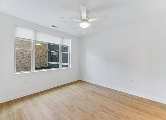 A room with a ceiling fan and a window overlooking a building.