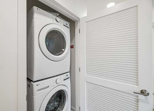 A white washing machine is stacked on top of another in a small laundry room.