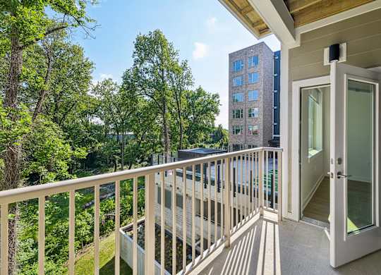 A balcony with a glass door leading to a room with a view of a tree-filled area.