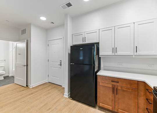 A black refrigerator is in a kitchen with white cabinets and a wooden floor.