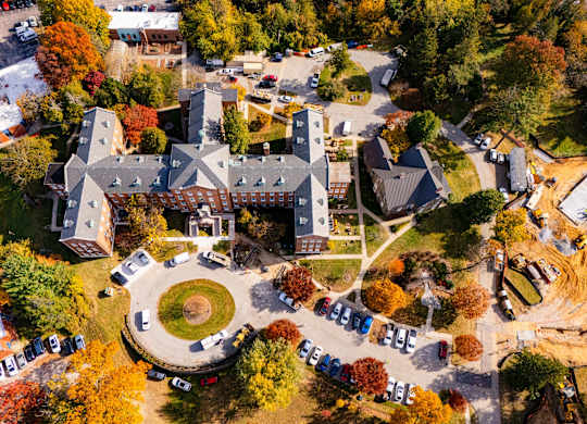 An aerial view of a campus with a large building in the center and a parking lot with cars.