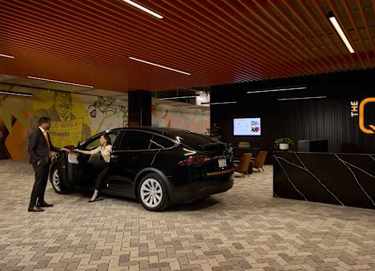A black car is parked in a showroom with a man standing beside it.