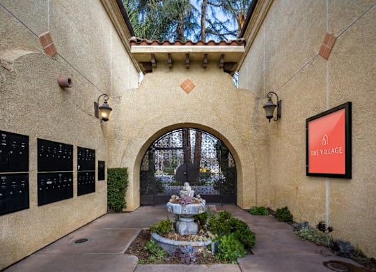 A stone archway leads to a courtyard with a fountain and a sign that says